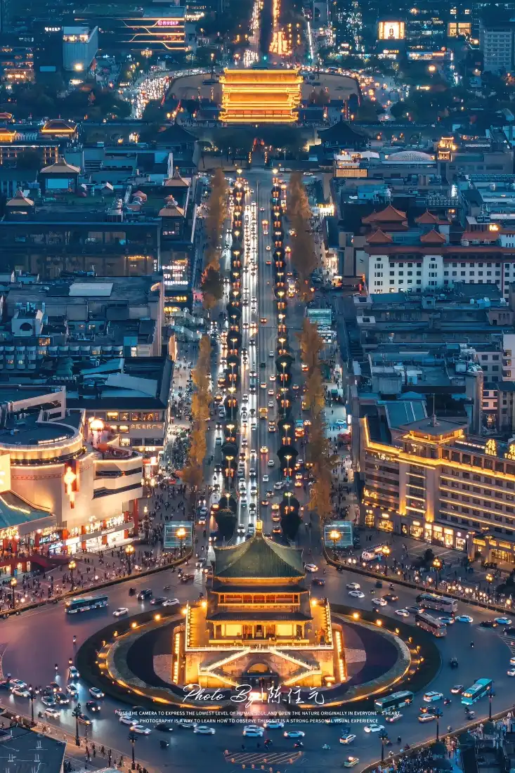 航拍西安钟楼夜景，暖光古建筑居中，街道车流与城市灯火沿中轴线延伸