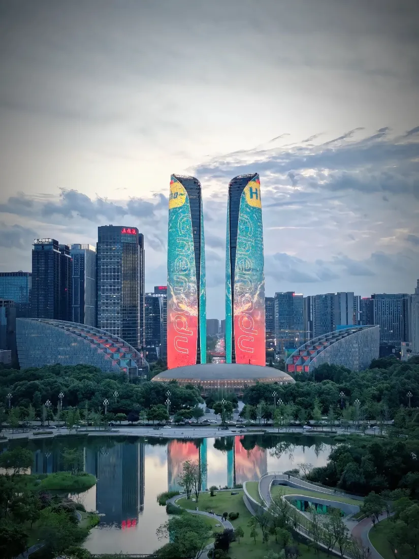 黄昏时分成都天府双塔亮灯，前方湖面清晰倒映双塔与城市天际线。