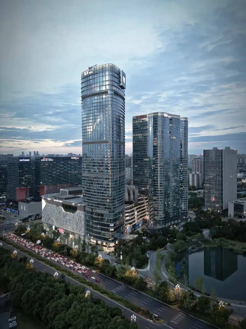 高空俯瞰成都商务区玻璃幕墙摩天楼群，下方道路车流与城市湖泊绿树环绕。