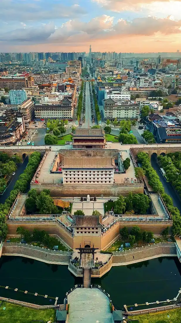 航拍西安城墙城门，护城河环绕，中轴线道路延伸至远处城市天际线。