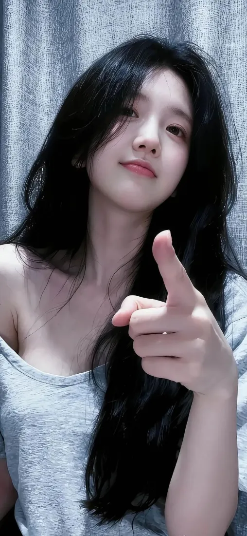 灰衣长发女生在灰色窗帘前自拍，抬手指向镜头，神态柔和。