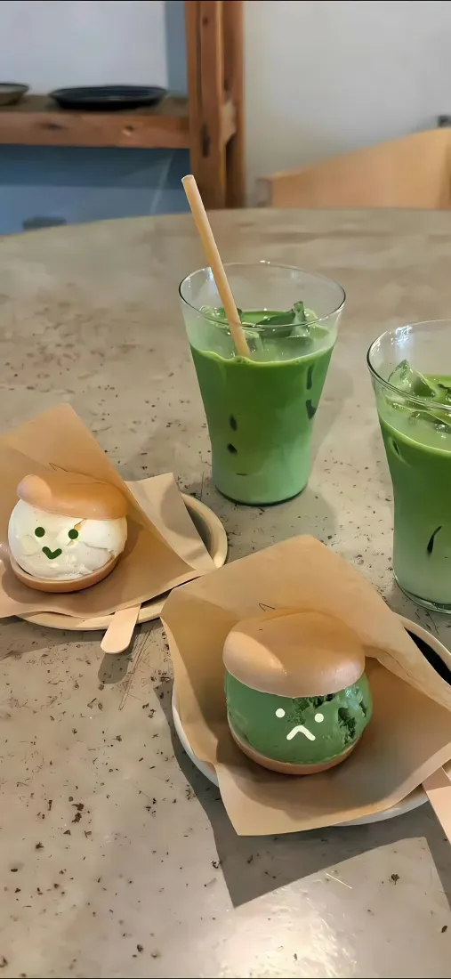 咖啡店桌面上摆放着两杯抹茶饮品和两款带可爱表情的猫咪造型点心