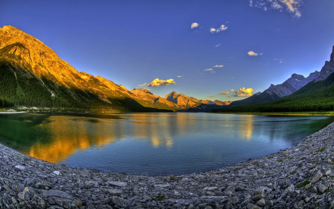 黄昏时分的山谷湖泊，左侧山峰被夕阳染成金橙色，湖面清晰倒映山影与蓝天。