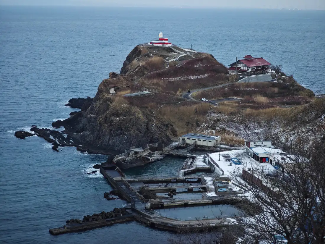 冬季覆雪的临海岩岛，山顶红白灯塔，下方港湾码头与沿岸小屋。