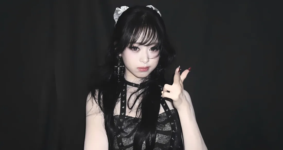 暗黑背景前，戴白色发饰、穿黑色蕾丝服饰的年轻女生比出俏皮手势。