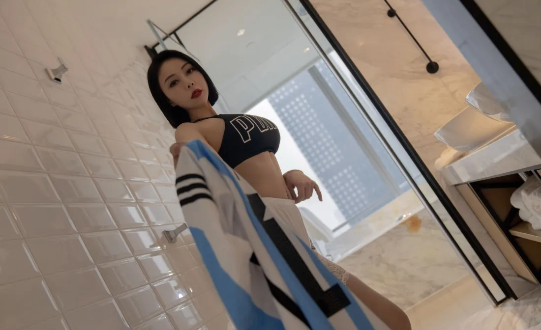 浴室瓷砖墙前，短发女子穿黑色运动内衣，手持条纹衣物摆拍。