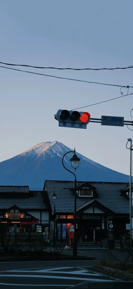 日式小镇街景，红灯亮起，远处富士山覆雪，蓝天澄澈。