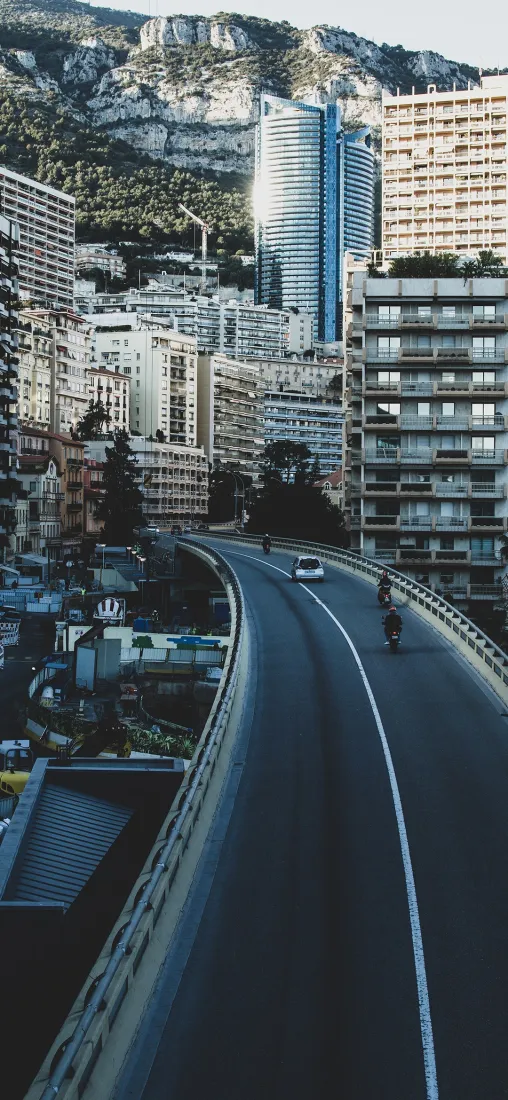 依山而建的密集都市建筑群，弯曲高架公路上有车辆与骑行者通行。