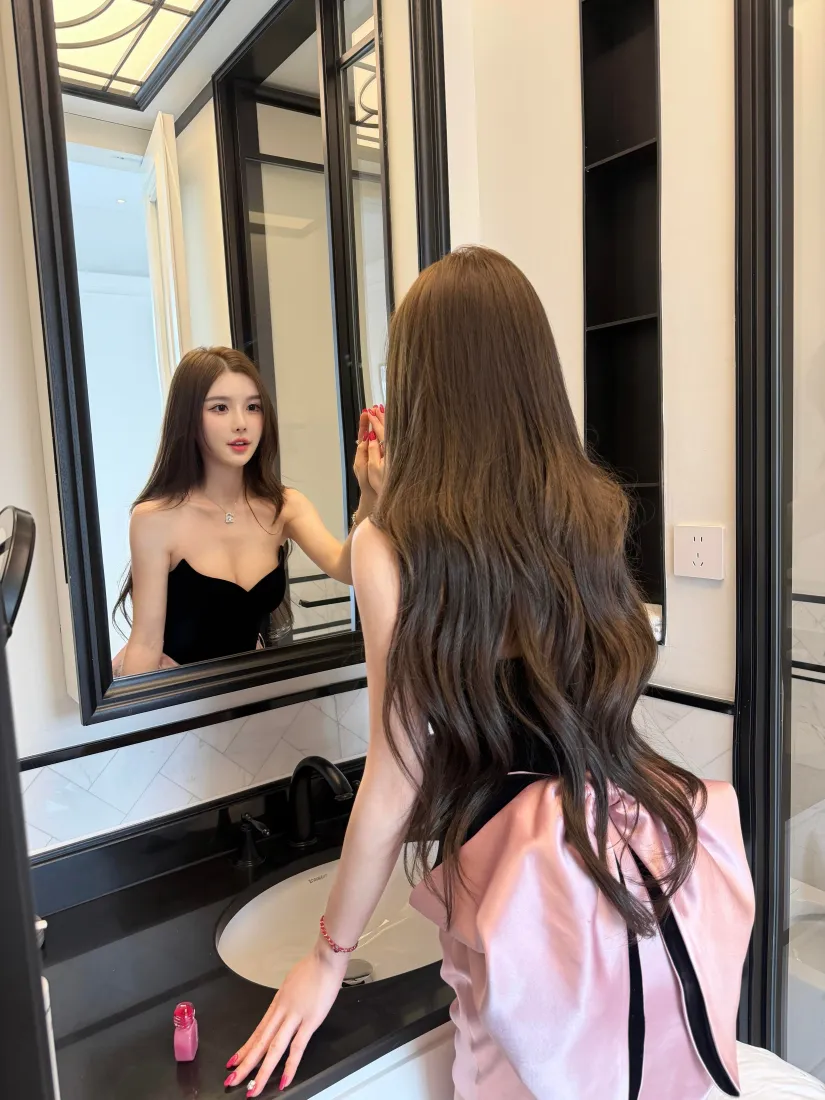 长发美女背对镜头在浴室镜前涂口红，镜中映出她穿黑色抹胸的正面