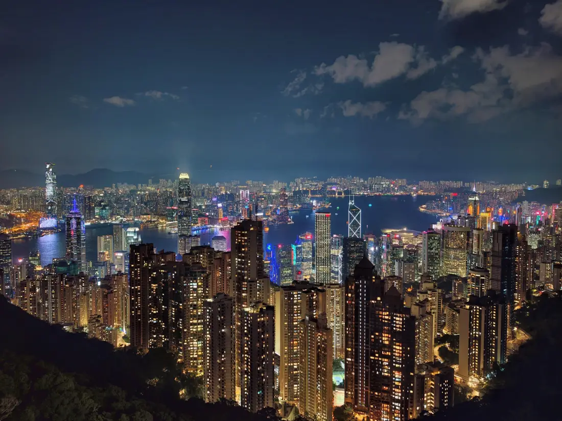 高空俯瞰的香港维多利亚港夜景，密集摩天楼灯火璀璨，夜空点缀薄云。