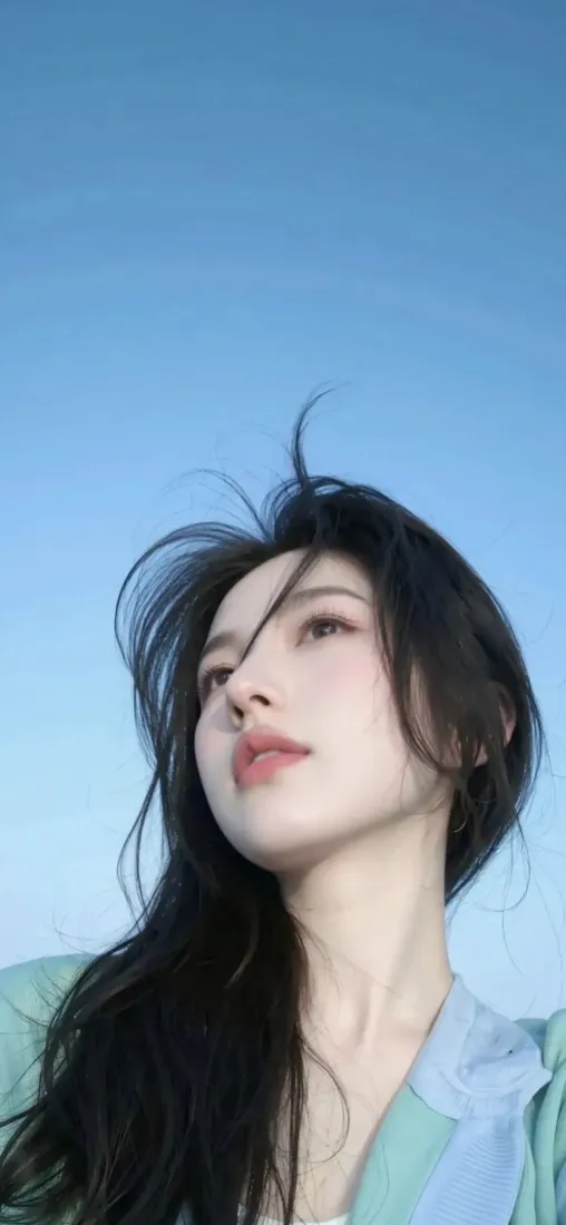 仰拍长发年轻女子，身着浅绿上衣，背景为纯净渐变蓝天。