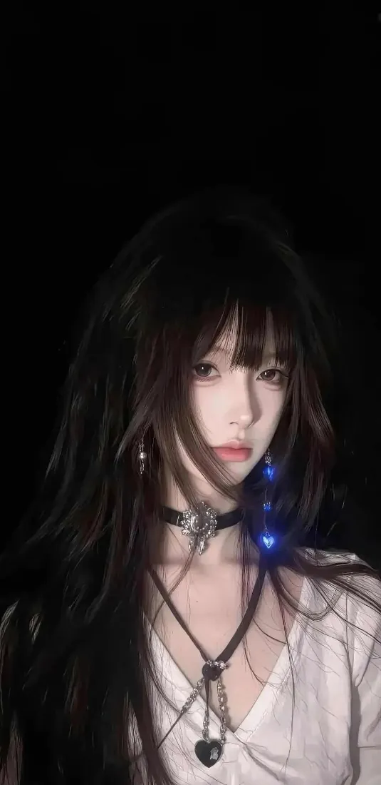 纯黑背景下，留黑长直齐刘海的年轻女性佩戴项圈与心形吊坠项链，身着白色上衣。