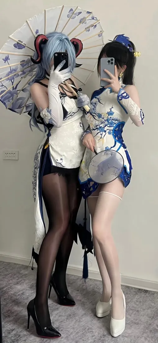 两名身着蓝白旗袍风格cos服的女性室内对镜自拍，分别持油纸伞与团扇。