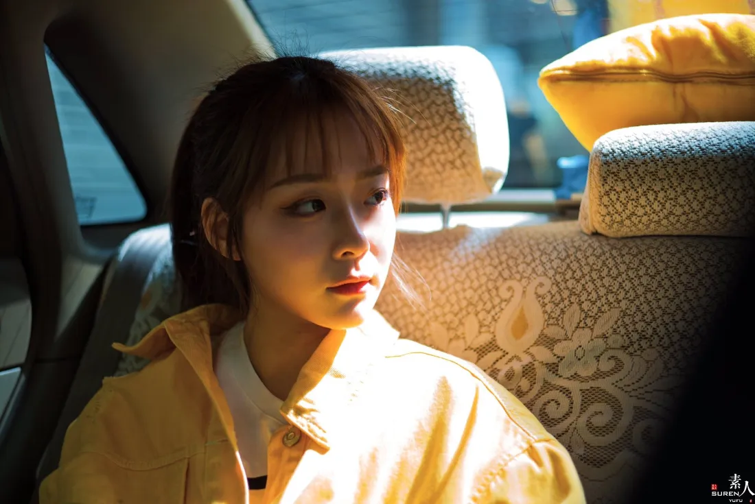 暖光下穿黄色外套的清纯女生坐在汽车后座，侧脸望向窗外。