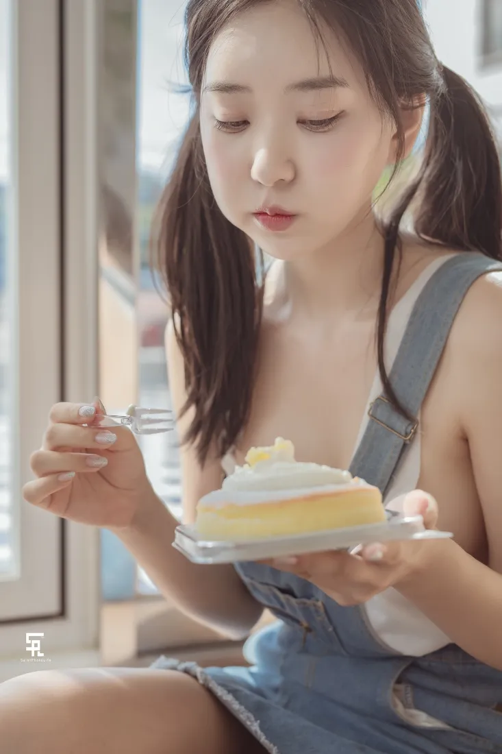 窗边双马尾少女穿牛仔背带裙，手持蛋糕与叉子准备享用