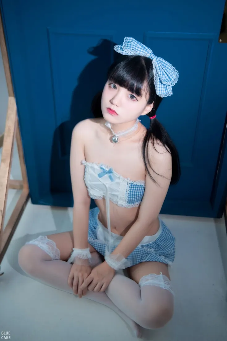 蓝白格纹蝴蝶结少女盘腿坐于蓝墙前，身着蓝白格纹服饰与白丝袜。