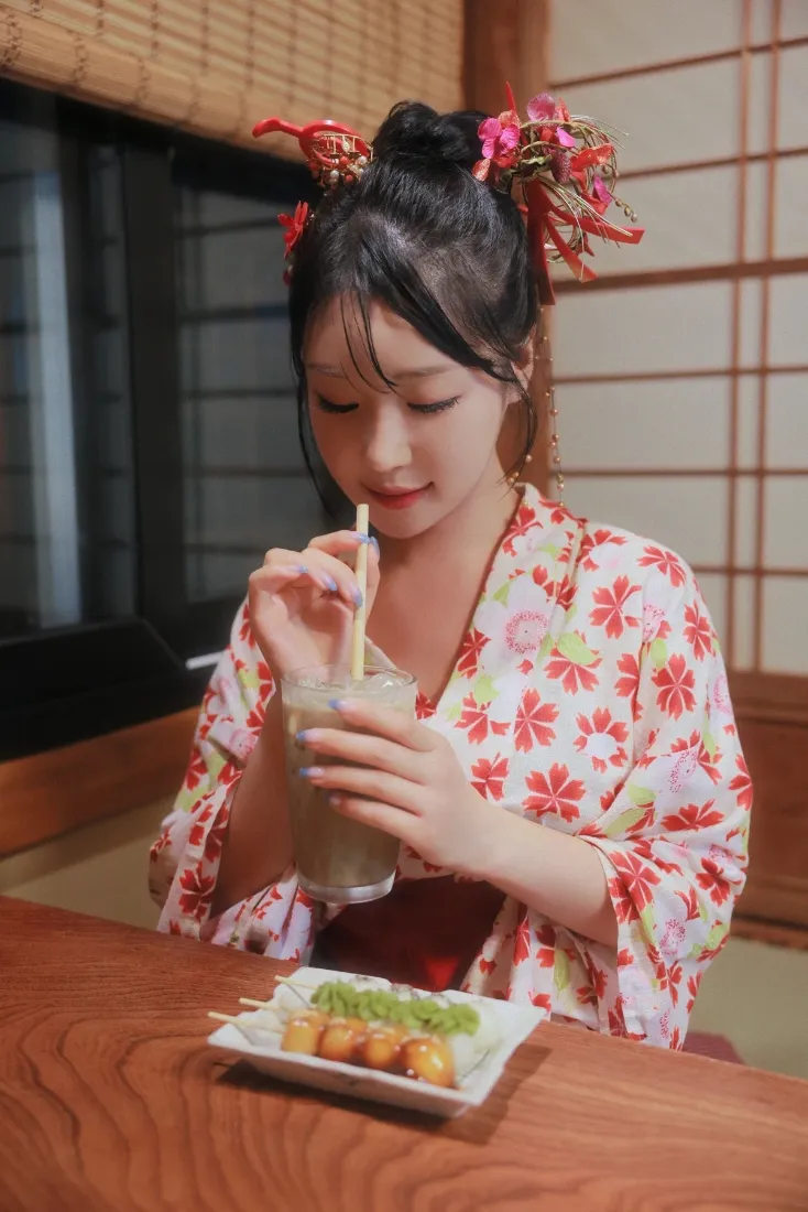 穿花型和服的女子在日式室内用吸管喝饮品，木桌摆放小吃