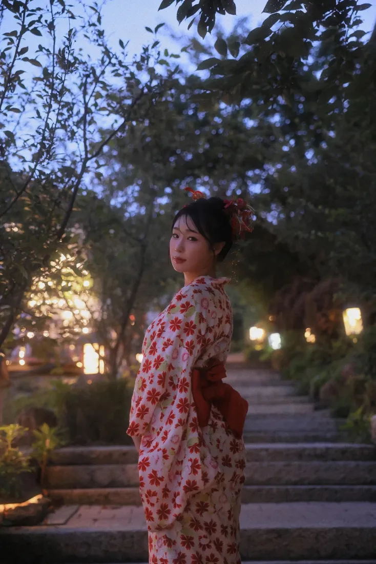 夜晚日式庭院中，身着红花和服的女子立于石阶旁，灯笼暖光环绕。