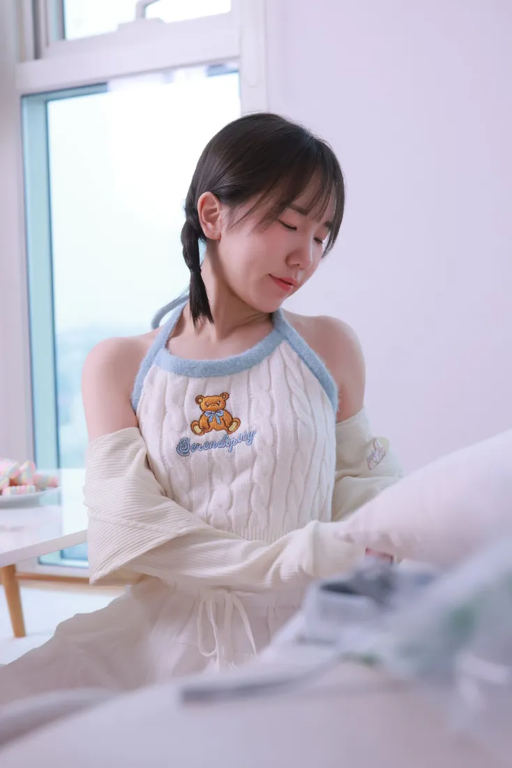 穿小熊图案露肩居家服的女生在窗边整理织物，氛围柔和温馨