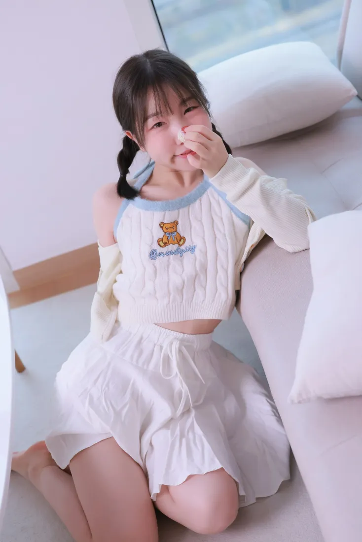 扎双马尾的少女穿小熊图案居家服，在沙发旁捂嘴俏皮微笑