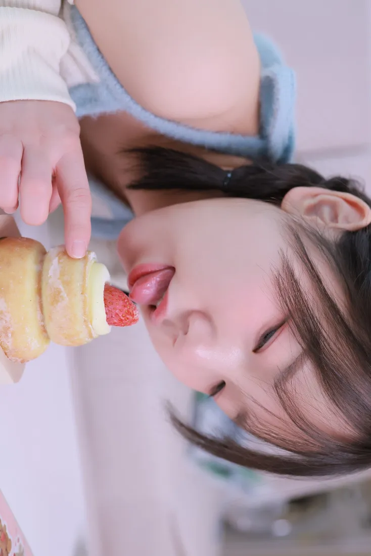 蓝白穿搭少女手持草莓奶油蛋糕卷，闭眼伸舌轻舔草莓的近景人像