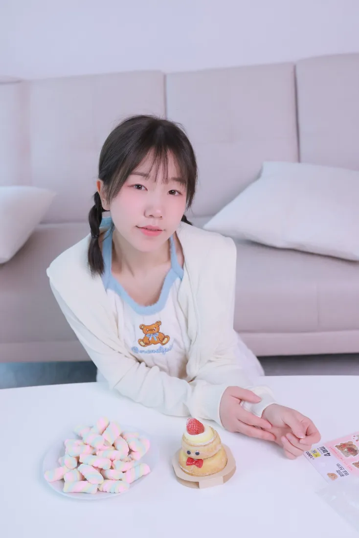 双马尾少女穿小熊上衣坐于桌前，桌上摆着棉花糖与小熊造型甜点。