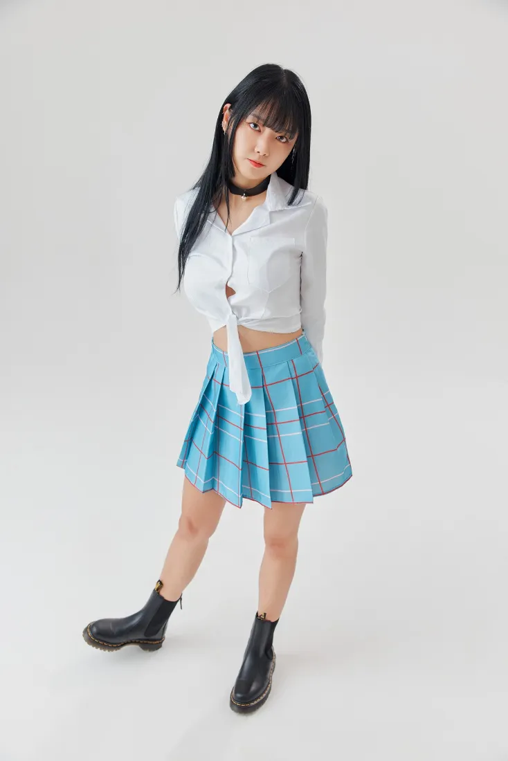 浅灰影棚内，黑发少女穿白衬衫蓝格百褶裙黑短靴站立写真