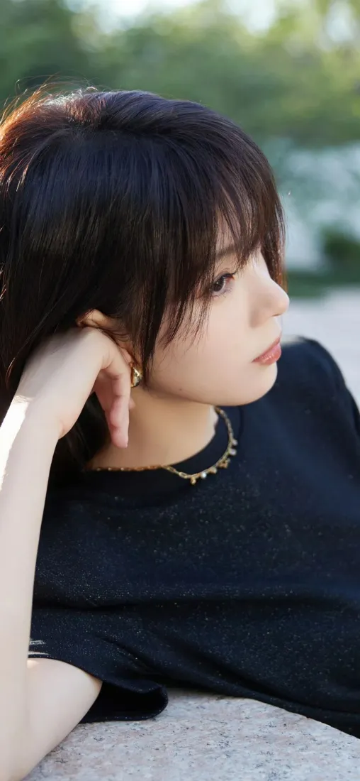 户外绿植背景下，短发黑衣美女侧脸托手，佩戴金色项链与耳饰。