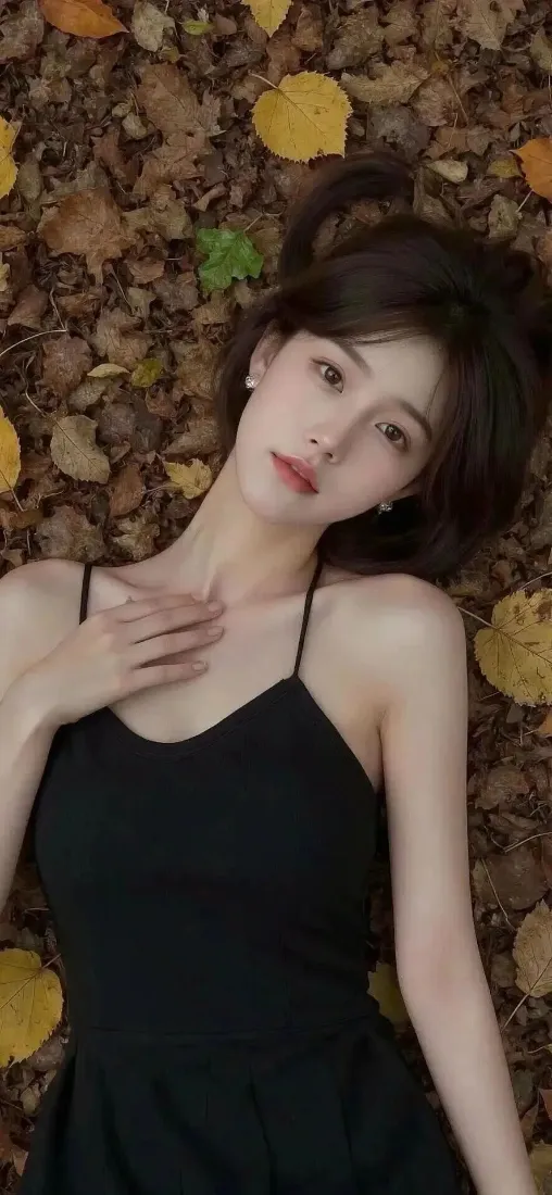 黑发女子身着黑色吊带裙，躺卧在铺满秋日落叶的地面上，姿态温柔。