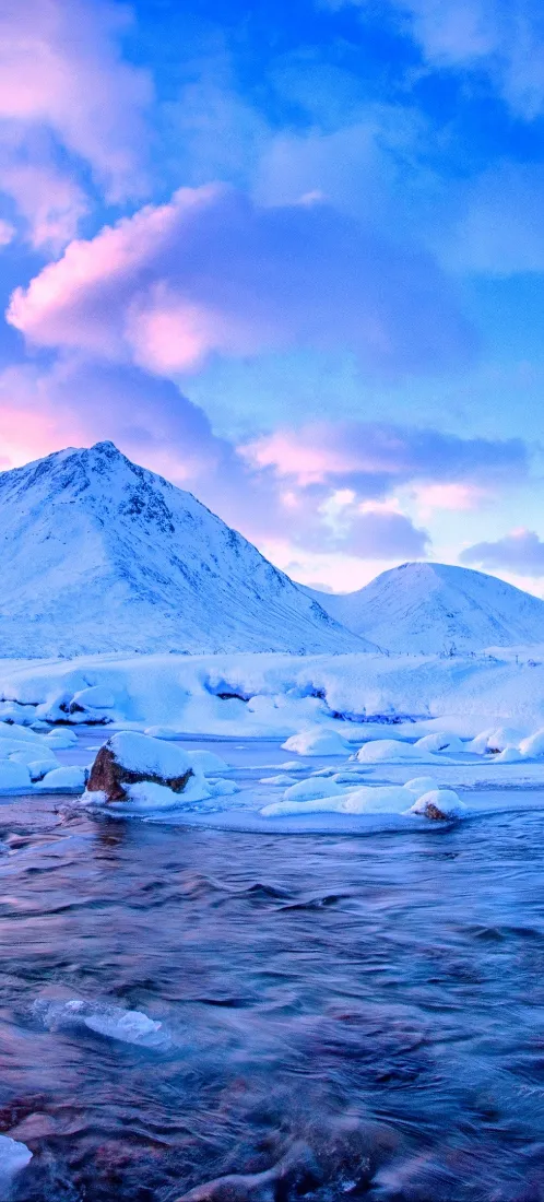 粉云蓝天之下，覆雪雪山矗立，冰湖浮冰散布的冬日极地风光