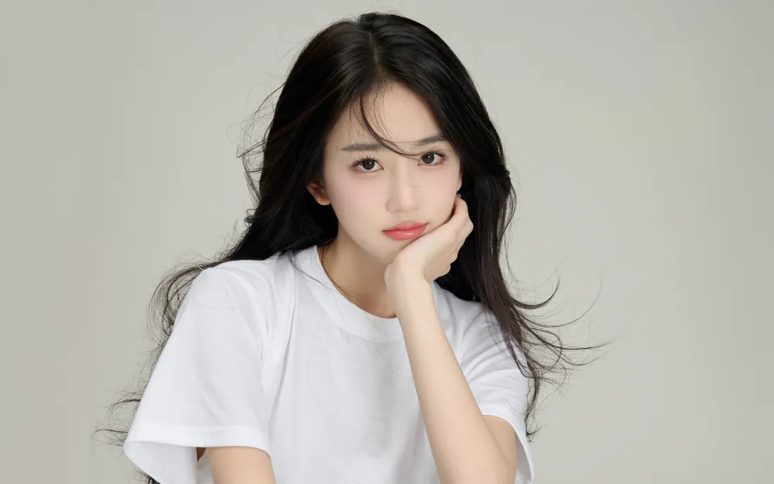 浅灰纯色背景下，黑长直长发少女穿白T恤，手托脸颊看向镜头。