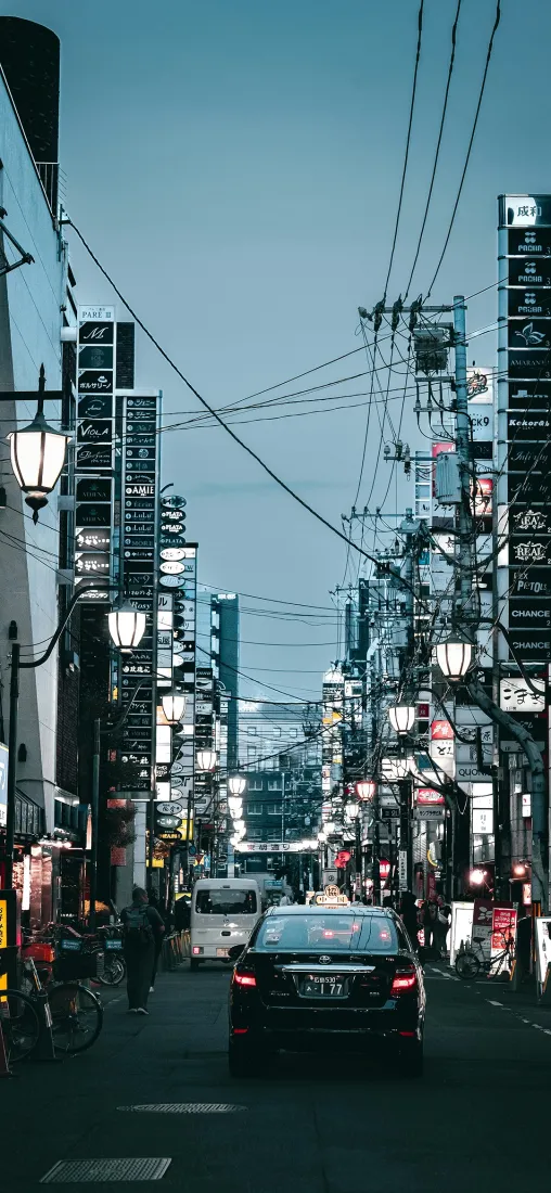 日式临街商业街，道路向远处延伸，两侧商铺林立，空中布满交错电线。