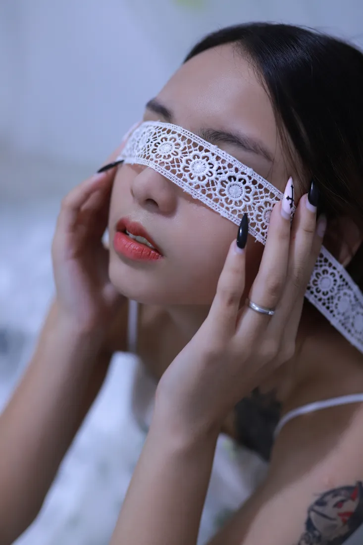 黑发美女以白色蕾丝绑带蒙眼，双手扶带，居家氛围感写真。