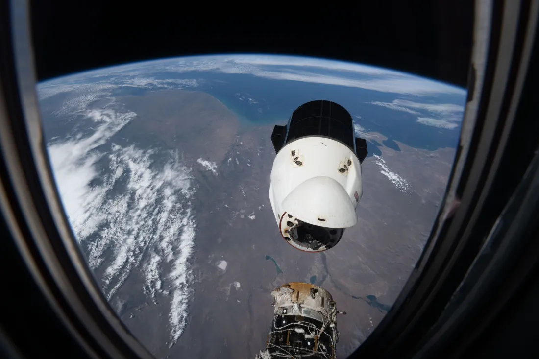 从空间站舷窗望向地球轨道，SpaceX载人龙飞船悬停在地球上方。