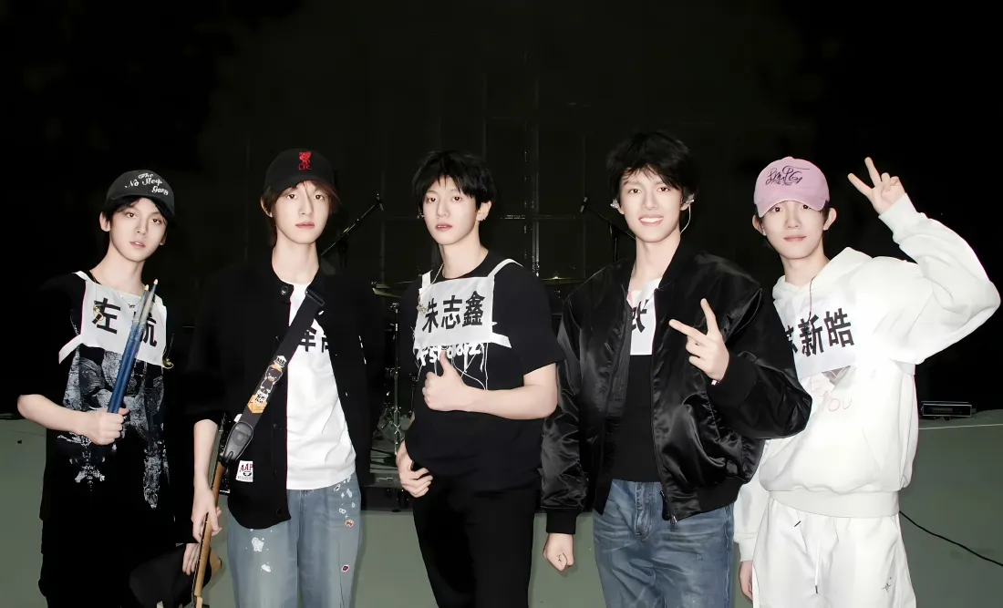 TF家族五名少年练习生在黑色背景的排练场地并排站立合影，部分比出手势。