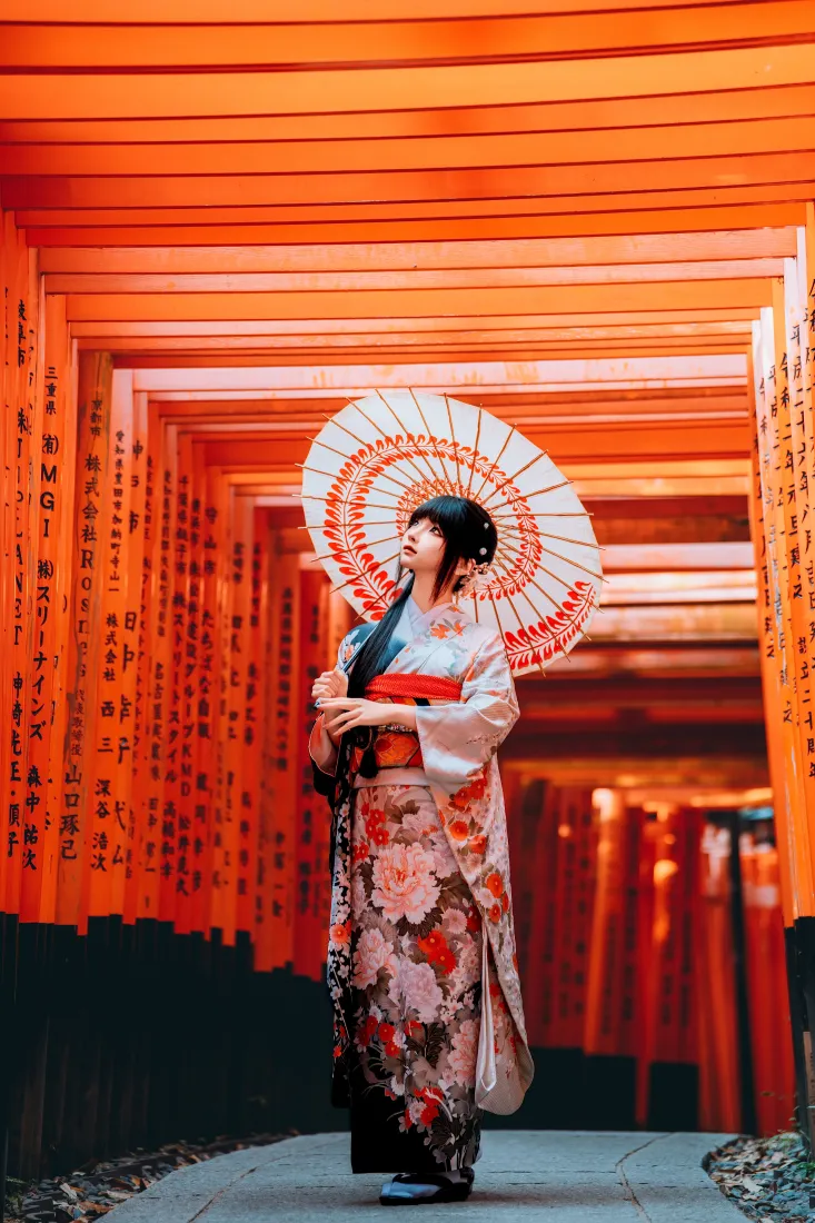 身着和服的少女持油纸伞站在伏见稻荷千本鸟居通道中。