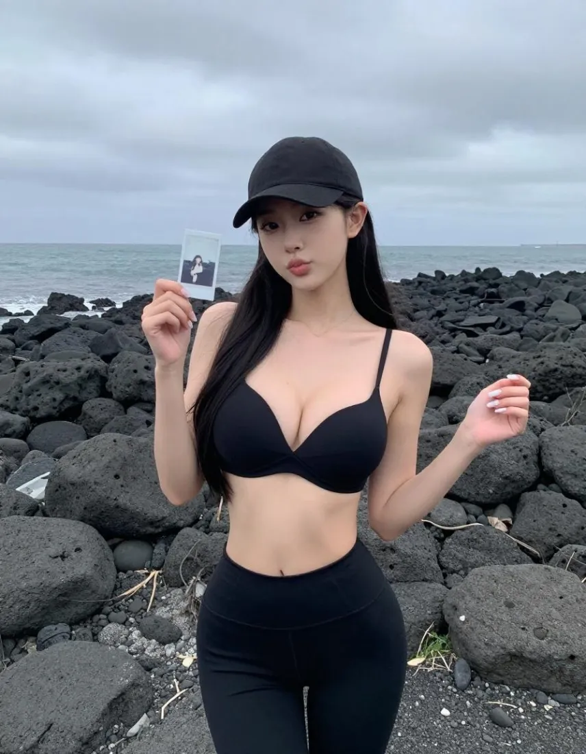 阴天海边黑礁石滩上，戴黑帽穿黑色内衣紧身裤的长发女子手持拍立得照片站立