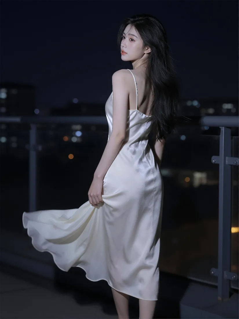 夜晚天台，穿白色吊带长裙的长发女子回眸，背景是虚化的都市夜景