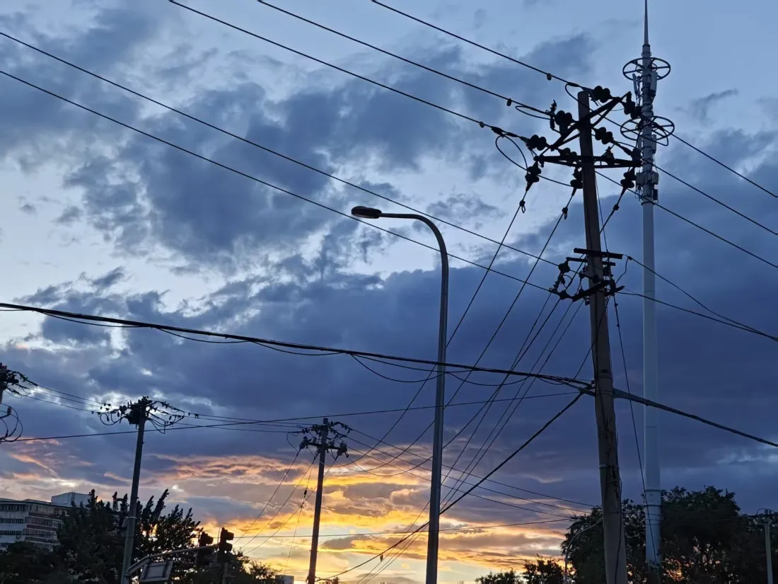 黄昏蓝调天空下，电线杆、路灯与电线构成的城市街景剪影。