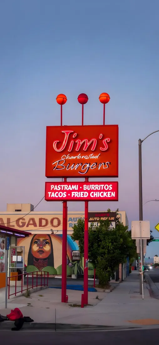 黄昏时分的美式街头，红色Jim's汉堡店招牌矗立在人行道旁，背景是渐变粉紫晴空。