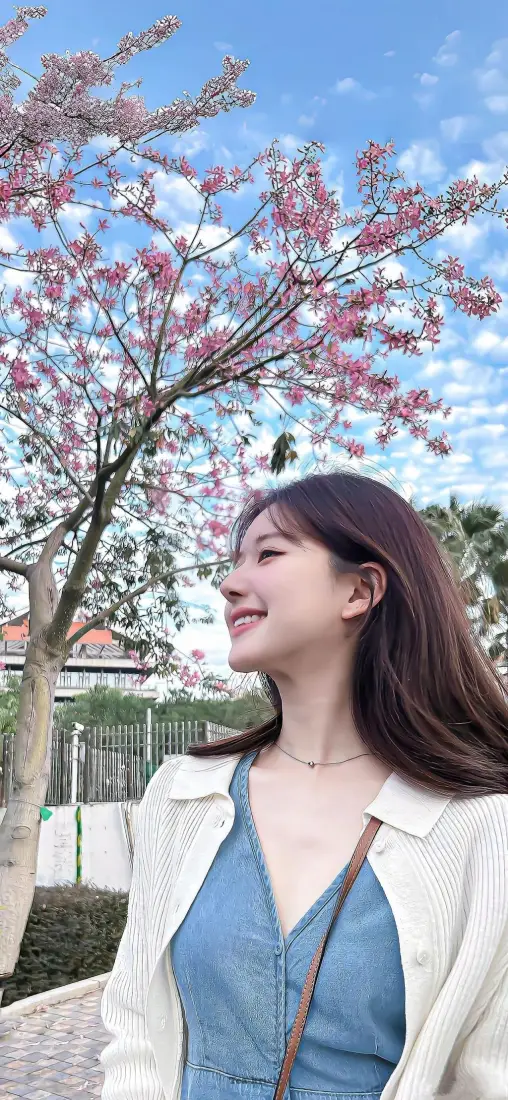 赵露思身着白外套蓝吊带，在樱花树下侧头微笑，背景是蓝天粉花。