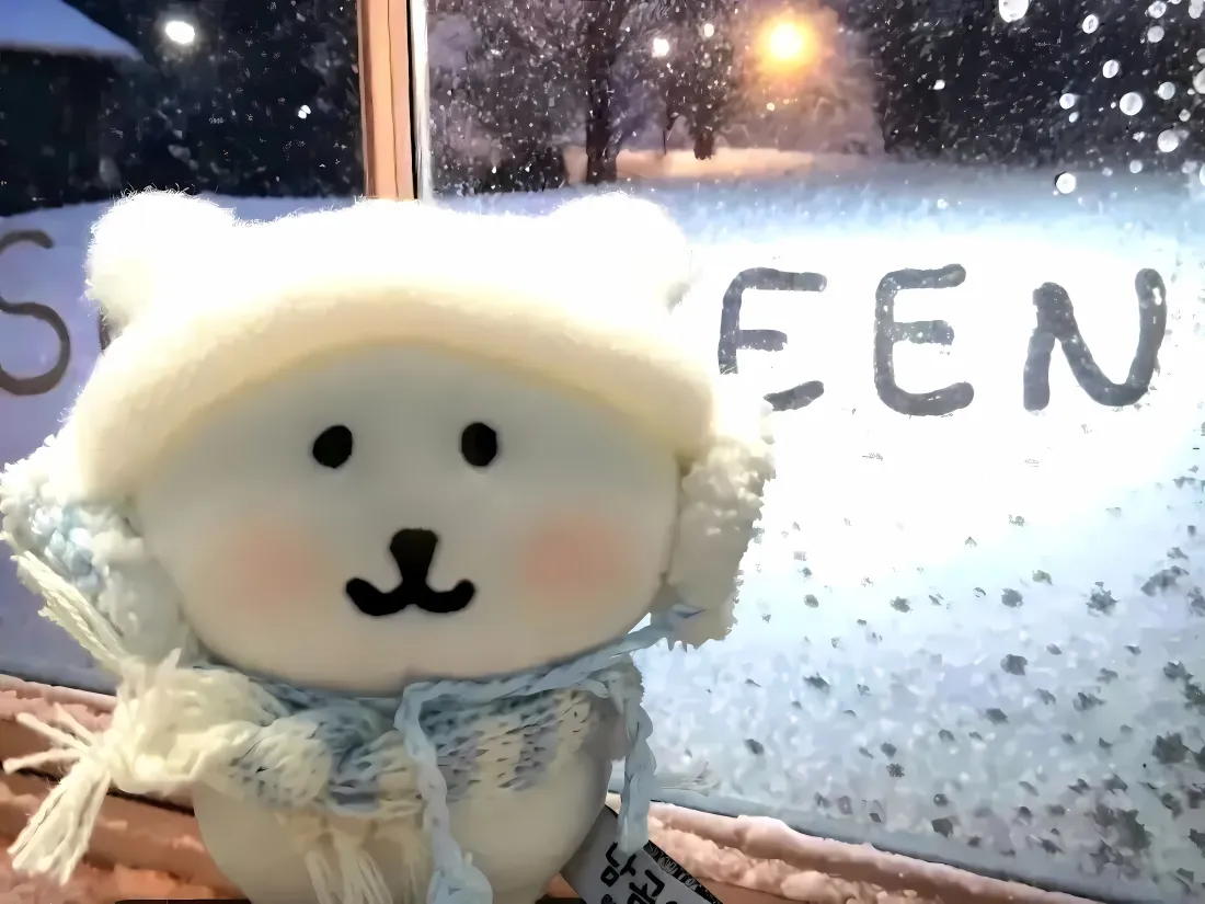 戴针织帽围巾的自嘲熊毛绒玩偶置于落雪的窗边，窗外是冬夜雪景