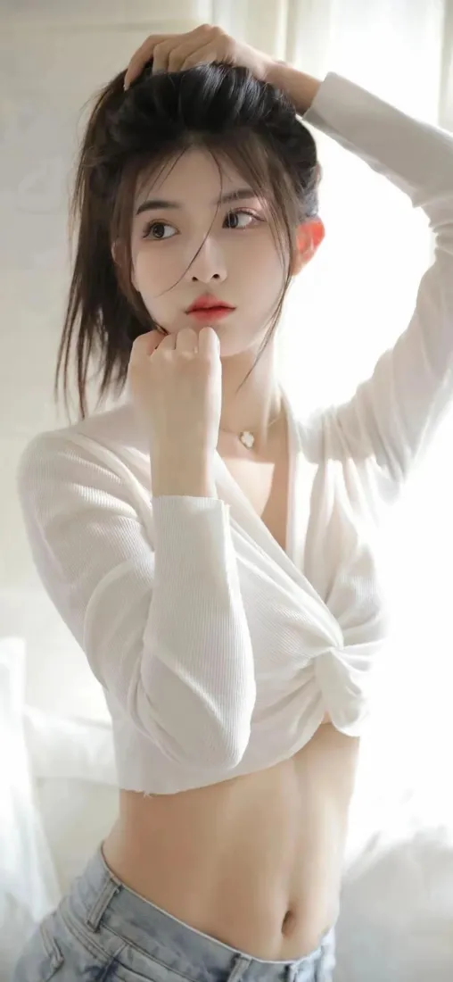 室内自然光下，穿白色短上衣牛仔裤的年轻女生抬手整理头发，氛围温柔清新。