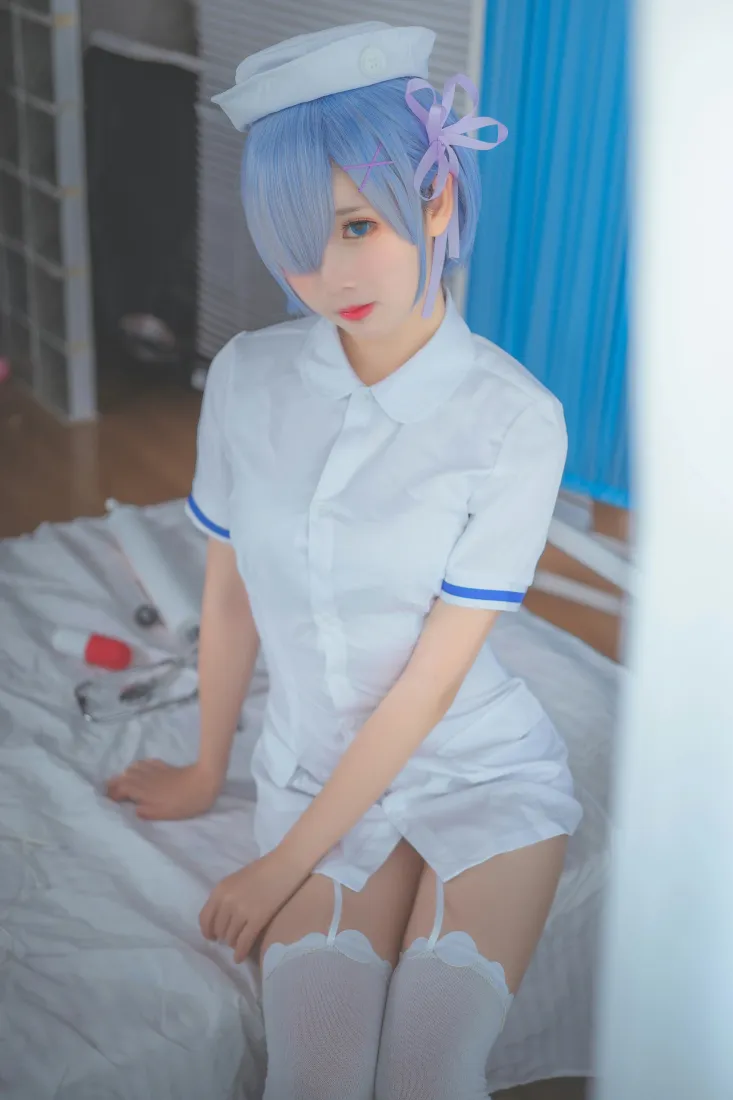 蓝发coser身着白蓝护士制服，坐在病房病床上，背景为蓝色隔帘。