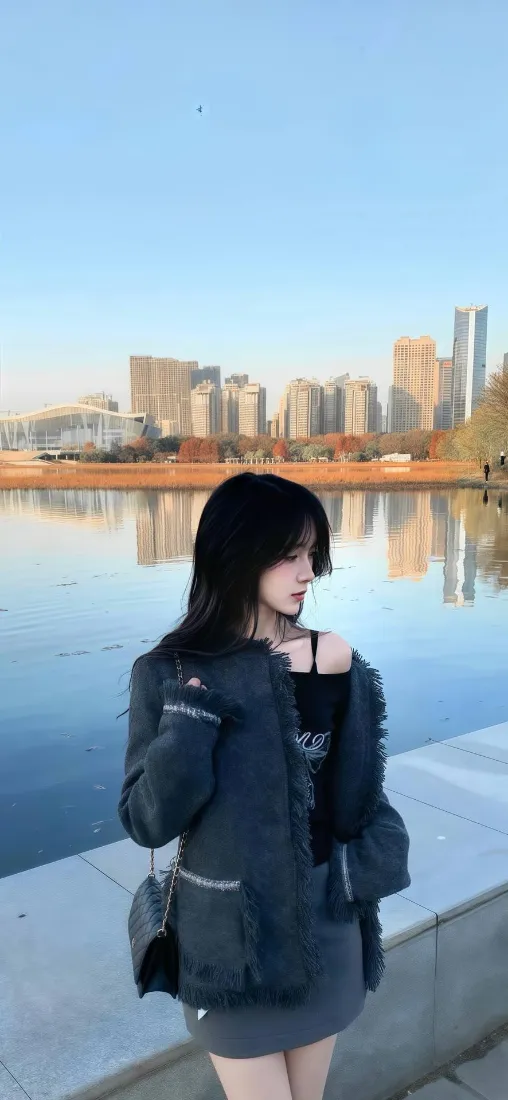 黑衣长发女生站在滨江步道，身后是平静江面与城市天际线倒影