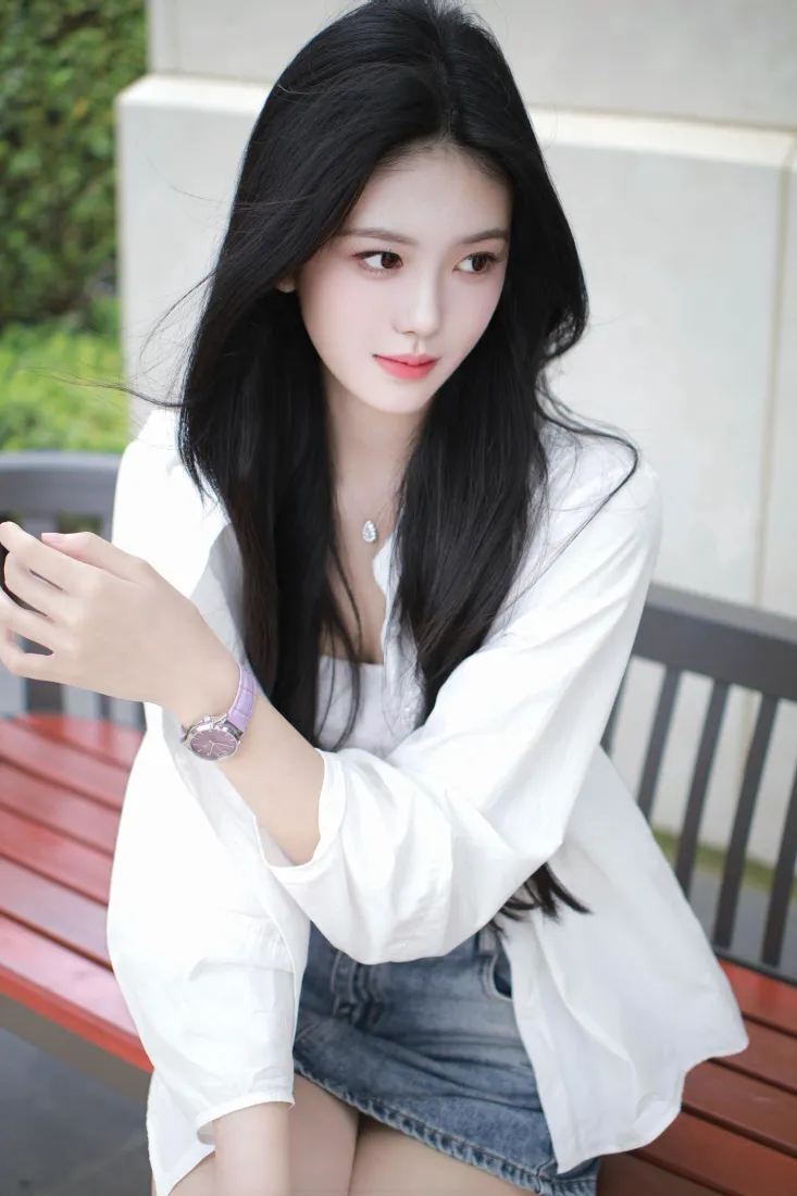 户外长椅上，黑长发白衬衫牛仔短裙的年轻女子手持手机，气质清新。