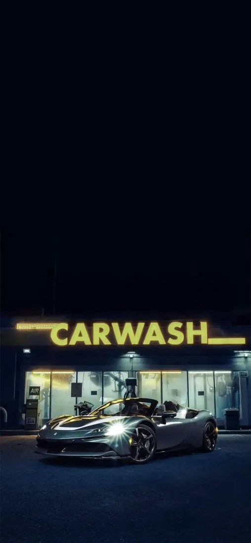 夜晚洗车店前停放着一辆银色敞篷超跑，上方亮着黄色CARWASH霓虹招牌