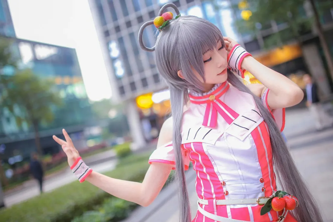 户外城市街景中，coser身着粉白洛天依服饰，灰长发比出手势闭眼摆拍。
