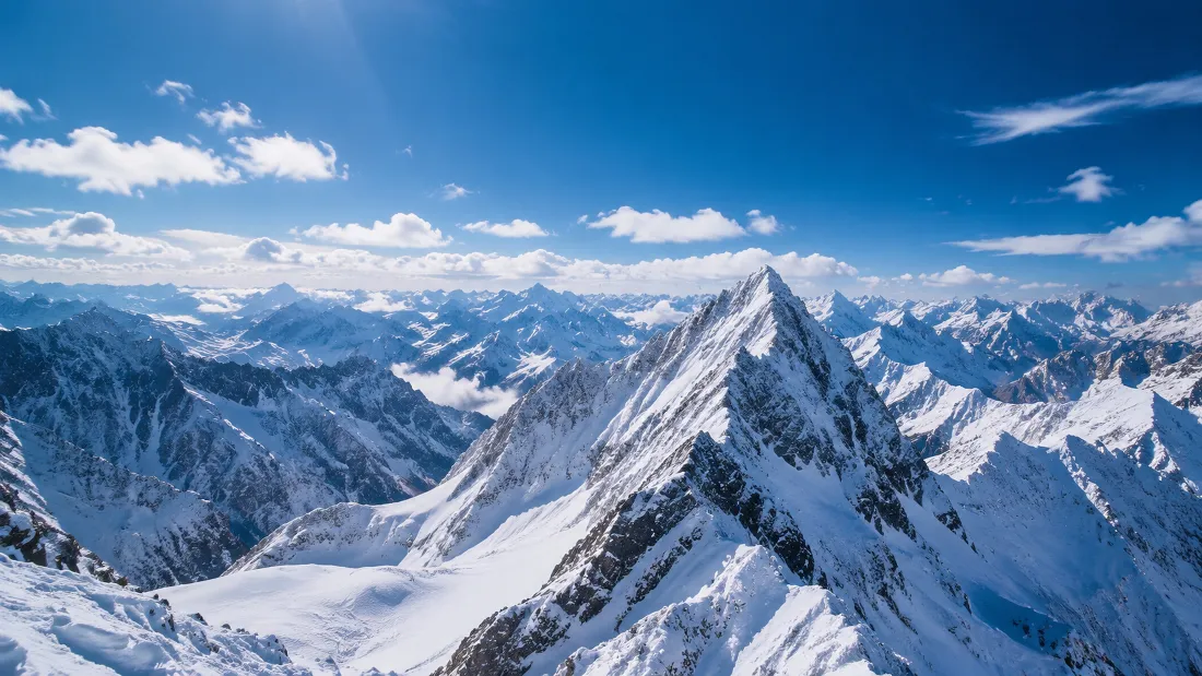 晴朗白日下，连绵积雪高原雪峰群在澄澈蓝天与白云映衬下壮阔延展。
