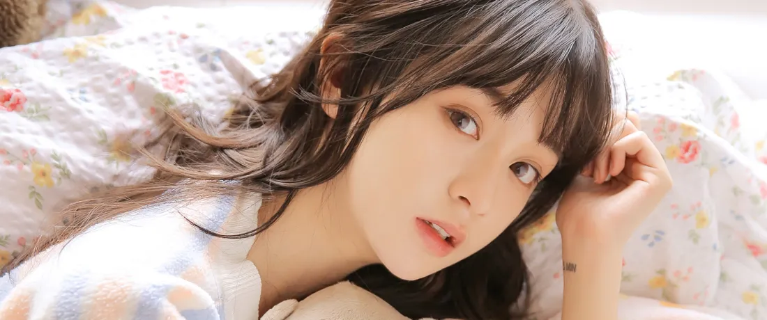 齐刘海长发清纯女生躺卧在碎花床品上，手轻扶头发看向镜头